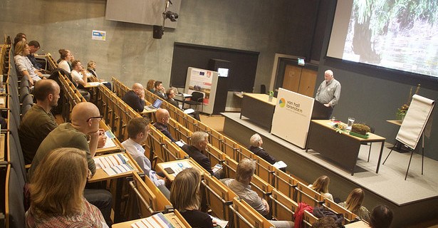 Socially distanced participants in a lecture hall, with Hans Joosten speaking at the front.