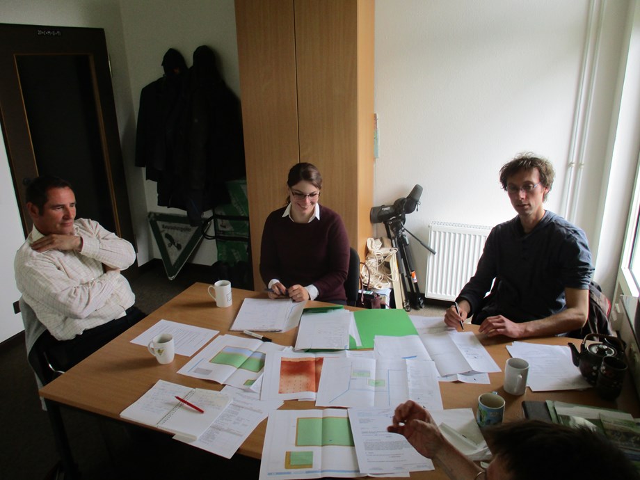 3 people gathered around a table covered in diagrams and paper.